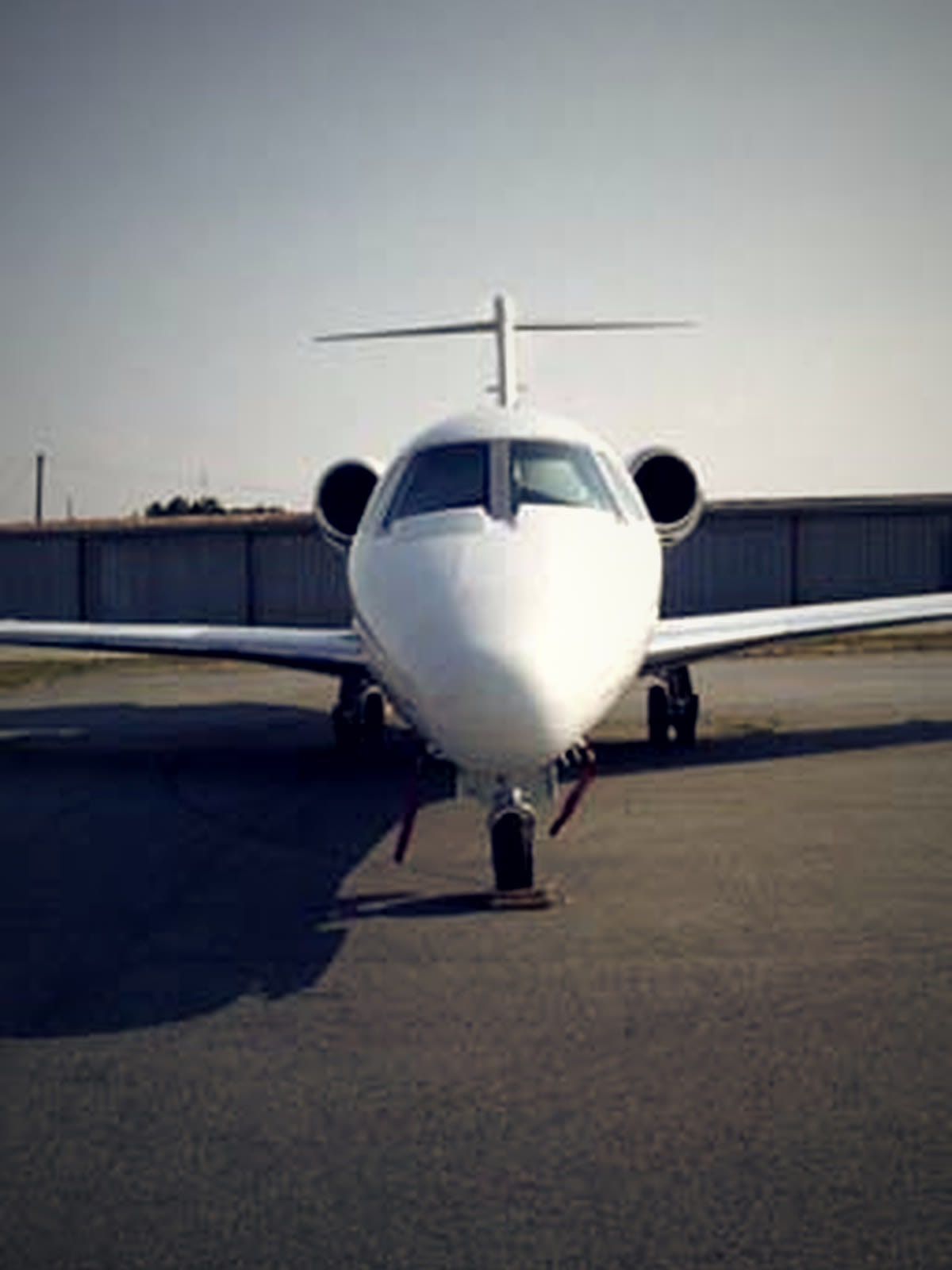 A business jet on the KTOC ramp with T-hangars behind it.